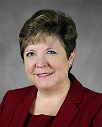 A woman with short dark blonde hair poses for a headshot swearing a red blazer.